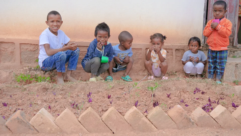 Children sitting beside a garden with young plants