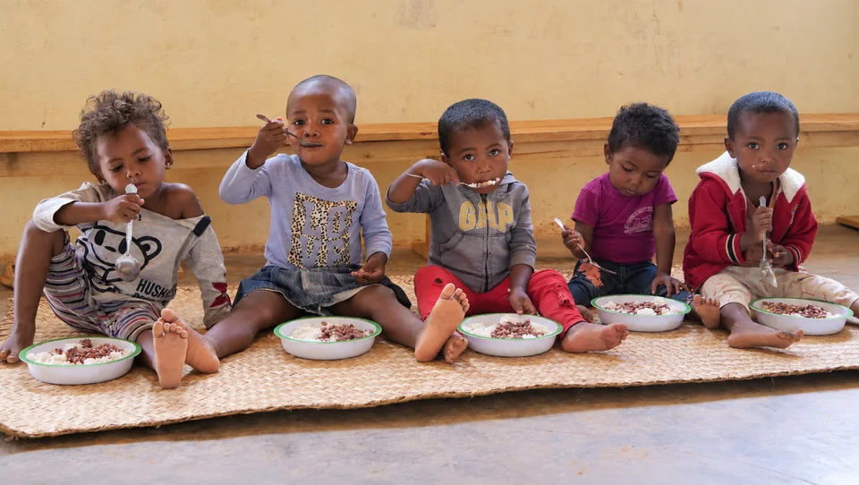 Children eating a meal while sitting on a mat