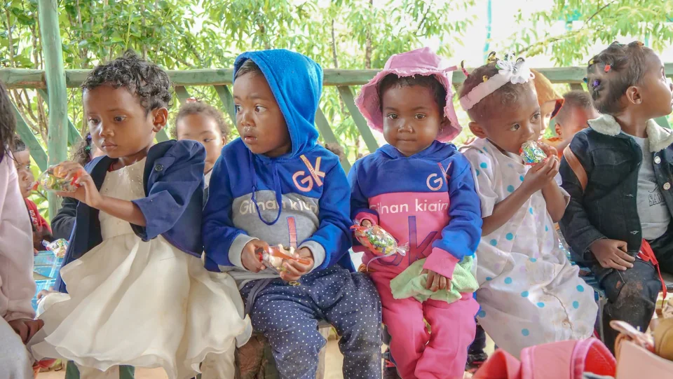 Children seated together outdoors under a shelter
